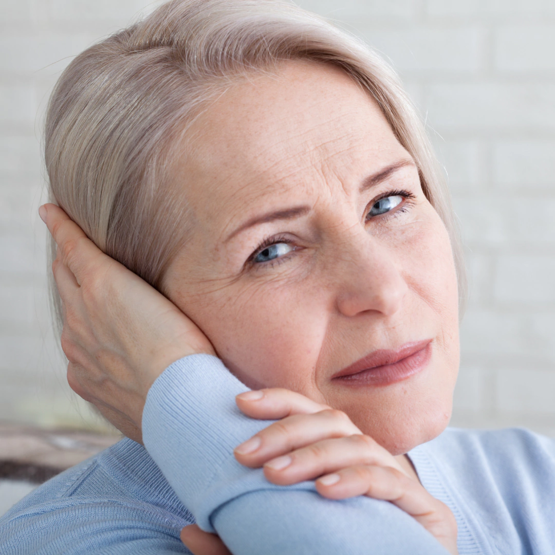Vrouw met grijs haar houdt haar hand tegen haar oor als gevolg van oorsuizen (tinnitus).