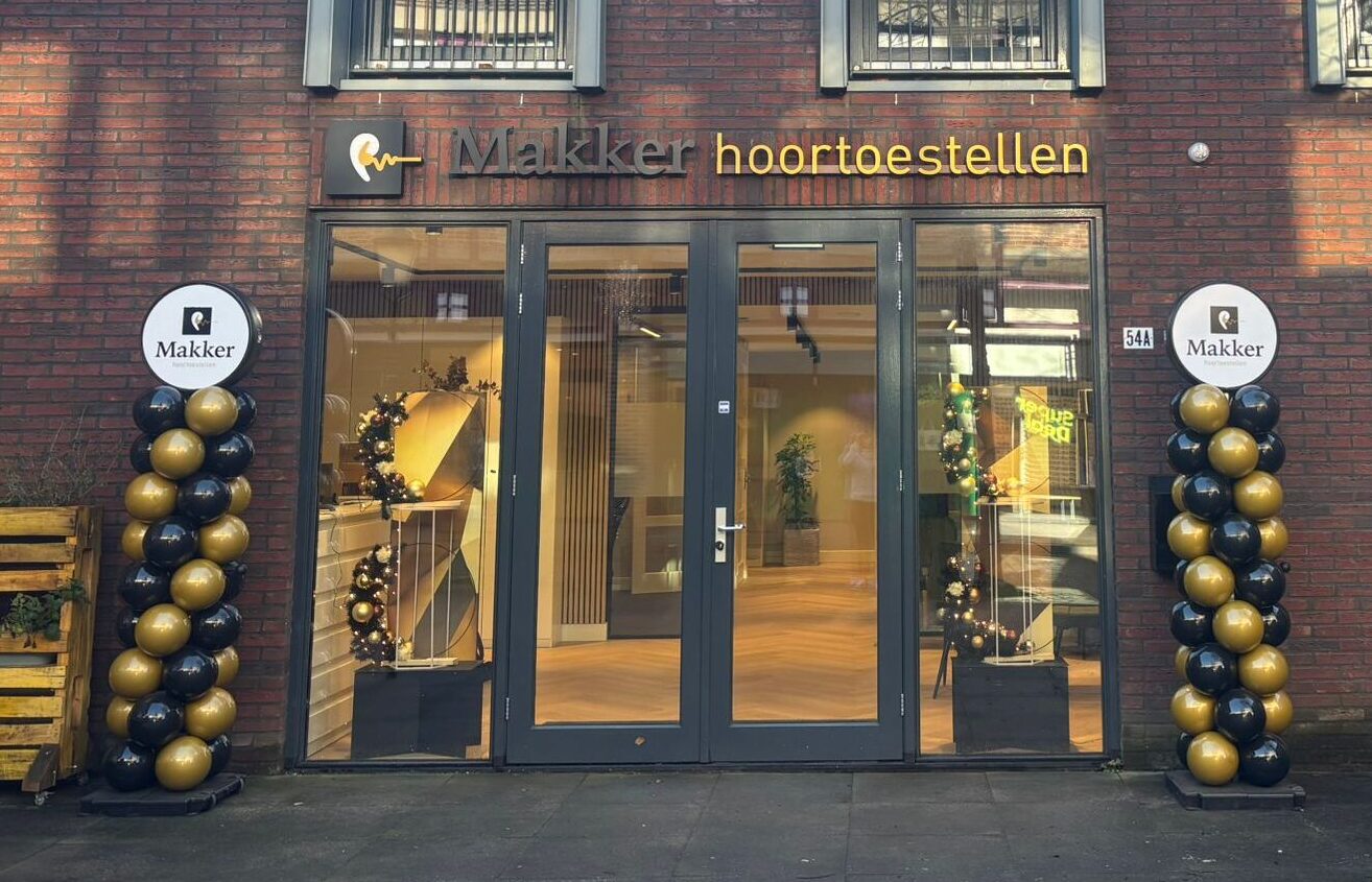 Vooraanzicht van de winkel van Makker Hoortoestellen met feestelijke zwart-gouden ballonnen bij de ingang.