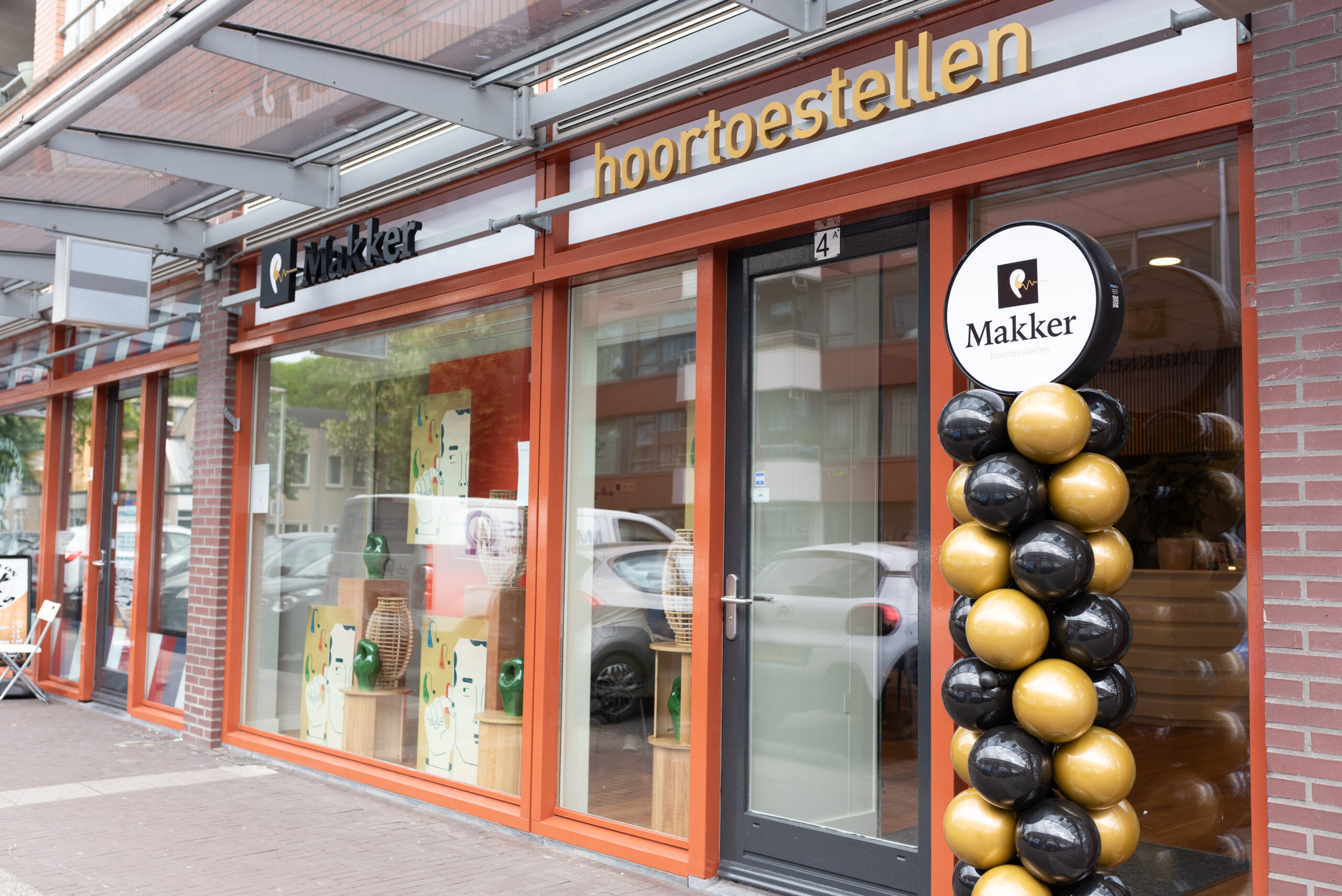 Vooraanzicht van hoorwinkel Makker Hoortoestellen met versiering van zwarte en gouden ballonnen bij de ingang.