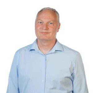 Portretfoto van Jan van Schaik in een lichtblauw overhemd tegen een witte achtergrond.