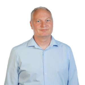 Portretfoto van Jan van Schaik in een lichtblauw overhemd tegen een witte achtergrond.