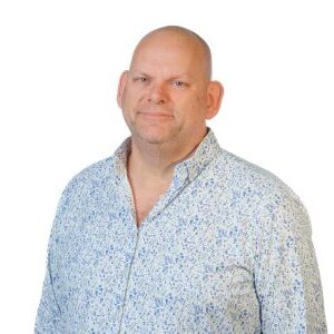 Profielfoto van een man in een lichtblauw met wit bloemenpatroon overhemd tegen een witte achtergrond.