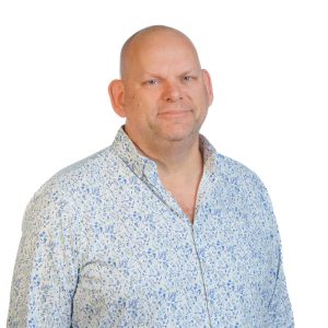 Profielfoto van een man in een lichtblauw met wit bloemenpatroon overhemd tegen een witte achtergrond.