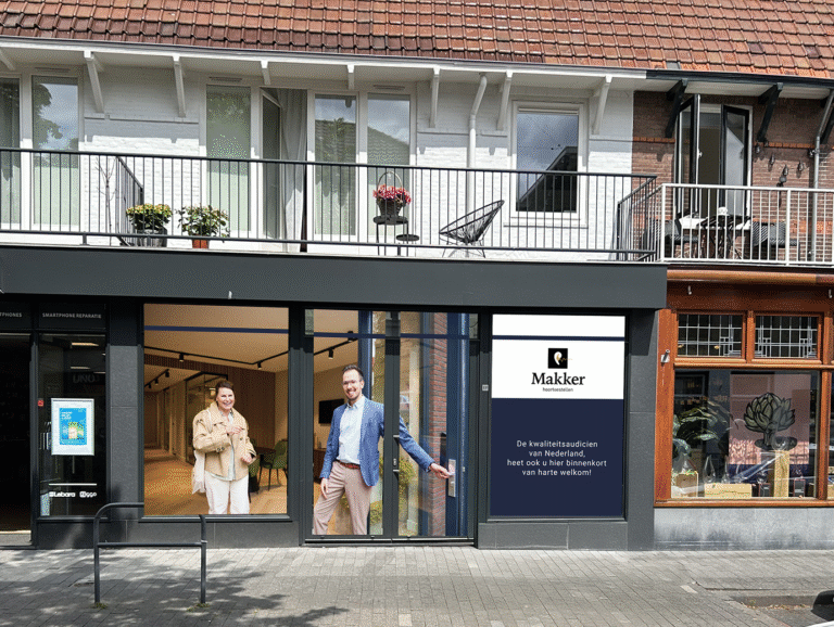 Gevel van Makker Hoortoestellen met twee lachende personen bij de ingang van de winkel.