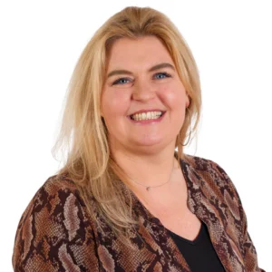 De afbeelding toont een lachende vrouw, Charlotte, met blond haar in een bruine blouse met slangenprint tegen een witte achtergrond.