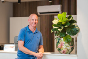 Glazen vaas met een groene plant op een bureau in een modern ingerichte ruimte met man in blauw shirt.