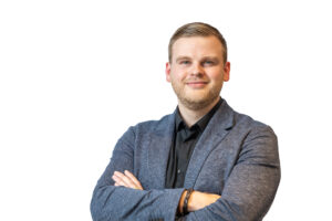Portret van een man in een blauw jasje en zwart overhemd met gekruiste armen tegen een witte achtergrond.