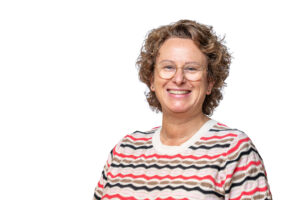 Portret van een lachende vrouw met krullend haar en een gestreepte trui tegen een witte achtergrond.