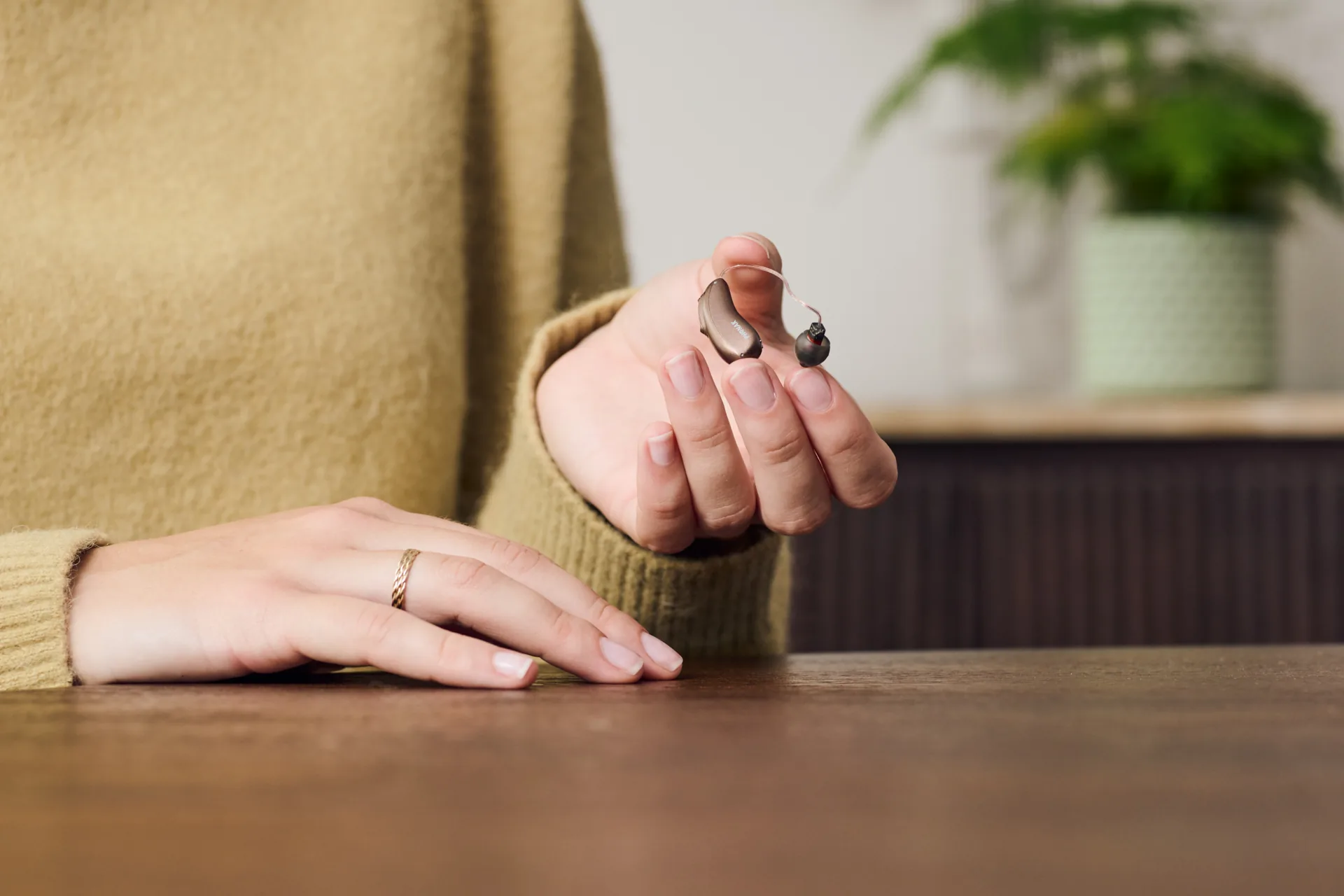 Vrouw houdt een klein hoortoestel tussen haar vingers